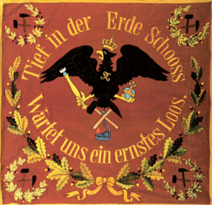 Historische Fahne in Braunrot mit einem schwarzen Reichsadler in der Mitte. Der Adler trägt eine Krone und hält einen Hammer und ein Bergbauwerkzeug.