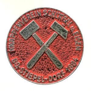 Silbern-rote Vereinsmünze mit gekreuztem Schlägel und Eisen (Bergbau-Symbol) auf rotem Grund, umlaufender Schriftzug „Knappenverein Schlägel u. Eisen – Bo-Stiepel-Dorf 1884“.