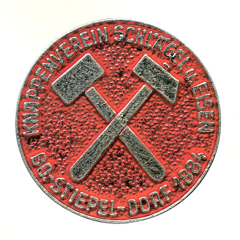 Silbern-rote Vereinsmünze mit gekreuztem Schlägel und Eisen (Bergbau-Symbol) auf rotem Grund, umlaufender Schriftzug „Knappenverein Schlägel u. Eisen – Bo-Stiepel-Dorf 1884“.